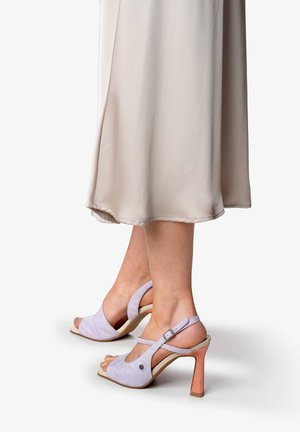 Sandali open-toe in suede viola con cinturino posteriore e tacco a blocco rosa chiaro. Presentano un piccolo dettaglio circolare sul lato esterno.