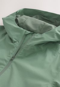 Hellgrüne Jacke mit hohem Kragen, ausgestattet mit einem vorderen Reißverschluss und glattem, mattem Stoff. Das Design ist schlank und mit minimalen Nähten gestaltet.