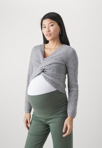 Grijze gebreide cardigan met gedraaide voorkant, lange mouwen, gecombineerd met een witte top en groene broek, geschikt voor zwangerschapskleding.