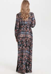Robe longue noire à fleurs avec des manches longues et une silhouette fluide, présentant des motifs complexes en bleu et rouge. Texture de tissu lisse.