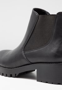 Mustat nilkkurit, joissa on sileä nahkapäällinen ja joustavat sivupaneelit, sekä paksu uritettu kumipohja lisäpidon takaamiseksi.