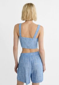Outfit coordinato in azzurro chiaro, composto da un top corto con spalline larghe e pantaloni corti larghi abbinati, entrambi realizzati in un tessuto strutturato.