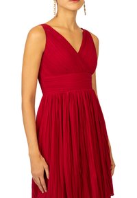 Robe plissée rouge avec un col en V et une taille cintrée, présentant une jupe fluide. Texture lisse avec des détails de drapés subtils.