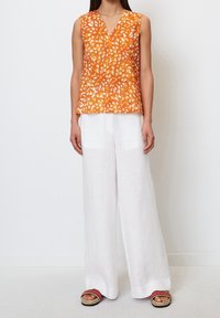 Blusa sin mangas naranja con patrón floral, diseño de escote en V, combinada con pantalones de lino blancos de pierna ancha y sandalias con acentos rojos.