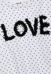 T-shirt blanc avec des pois noirs, met en avant un appliqué texturé en noir portant le mot "LOVE". Encolure ronde et manches courtes. Tissu en coton doux.