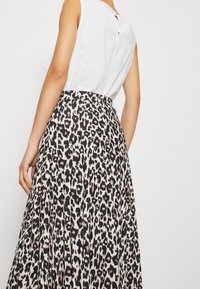 Falda maxi con estampado de leopardo en tonos negros, beige y rosa. Presenta pliegues y una cintura ajustada. Top blanco sin mangas con detalle de botón en la espalda.