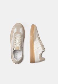 Zapatillas de ante beige y cuero blanco con suela de goma, que presentan un diseño clásico de cordones y sutiles acentos de logo.