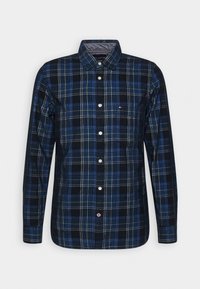 Koszula w kratę z długim rękawem w kolorach ciemnoniebieskim, jasnoniebieskim i czarnym. Posiada zapinany na guziki przód, kołnierz oraz pojedynczą kieszeń na piersi z logo.