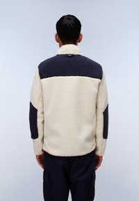 Cream and navy fleece jacket with a high collar, featuring a color-block design and textured fabric. Includes contrasting shoulder patches.
