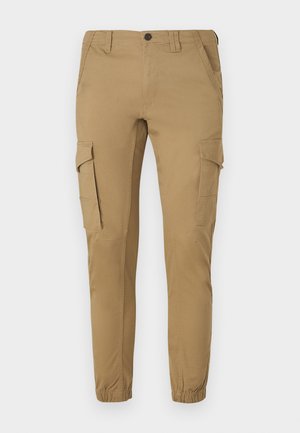 Krémszínű cargo nadrág, tapered szabással, két oldalsó zsebbel, két cargo zsebbel, és rugalmas mandzsettákkal a bokákon.