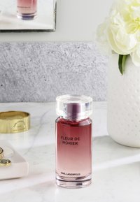 Glass fragrance bottle featuring a gradient from deep pink to clear at the base, with a transparent cap and black text on the label.