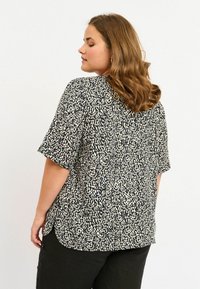 Blusa a maniche corte in stampa animale nera e crema, caratterizzata da una vestibilità comoda e un orlo arrotondato per maggiore comfort. Il tessuto morbido aggiunge texture.