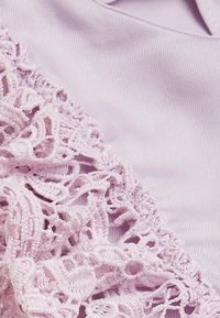 Lawendowy materiał z misternymi koronkowymi detalami po jednej stronie. Koronka ma płynny, falbaniasty wzór oraz miękką fakturę.