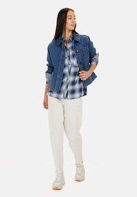 Denim jack, blauw, met een patch pocket; lichtblauw en wit geruit overhemd; crèmekleurige broek; lichte sneakers met witte en beige accenten.