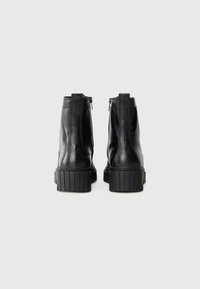 Botas de tobillo de cuero negro con suela de goma gruesa, cremalleras laterales y textura suave, con detalles de costura vertical.
