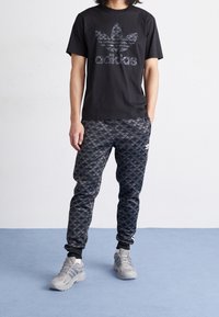 Svart t-shirt med en stor grå Adidas-logotyp. Grå och svart mönstrade joggers med Adidas-logotypen på underbenet. Ljusgrå sportskor.