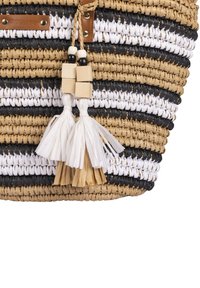 Sac en paille tressée avec des rayures noires, blanches et beige alternées. Comprend des pampilles en matériau blanc et beige avec des accents en bois.