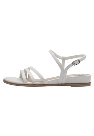 Des sandales plates blanches présentent plusieurs fines brides, une boucle de cheville ajustable et une semelle lisse avec une apparence naturelle de bois.