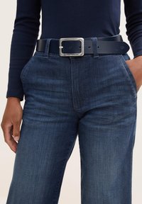 Dunkelblaue Jeanshose mit geradem Bein, kombiniert mit einem breiten schwarzen Leder-Gürtel mit einer silbernen quadratischen Schnalle.