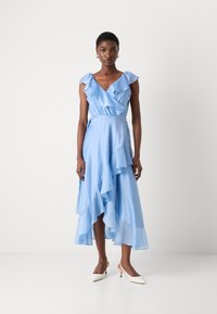Light blue dress with ruffled neckline and layered skirt. Smooth fabric flows to mid-calf. Styled with white pointed-toe heels.