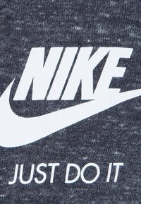 Grått tyg med ett texturerat stickat mönster som har en stor vit Nike-logotyp och sloganen "JUST DO IT" tryckt nedanför i en fet, modern font.
