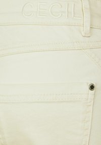 Białe dżinsy z fakturowanym wykończeniem, z przeszytym logo „CECIL” na pasku oraz srebrnym ćwiekiem na tylnej kieszeni.