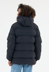 Schwarze Daunenjacke mit Kapuze, ausgestattet mit einem gesteppte Design und auffälligen Nähten. Das Modell trägt hellblaue Jeans.