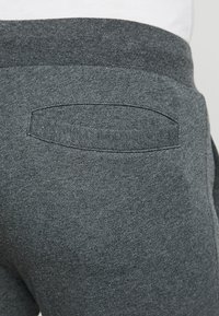 Pantaloni della tuta grigi con una tasca posteriore piatta e bordi superiori arrotondati. Realizzati in un morbido tessuto testurizzato con cintura elastica.