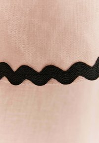 Detailný záber na svetloružovú tkaninu s čiernym vlnitým okrajom, ktorý ukazuje textúru a šitie.