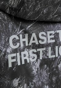 Nærbillede af sort stof med hvidt abstrakt mønster og delvis hvid tekst, der læser "CHASE FIRST LIC" i fede versaler.