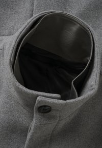 Colletto di cappotto in lana grigia con un bottone nero, fodera interna liscia e tasca, che mostra un design pulito e minimalista.