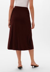 Gonna midi bordeaux con una texture liscia, caratterizzata da una vita alta e una silhouette fluente, abbinata a sandali con tacco marroni.