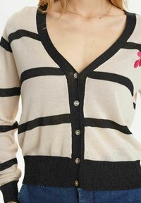 Beige cardigan with black horizontal stripes, V-neck, five-button closure, ribbed cuff, and hem; features pink floral embroidery on left side.