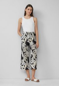 Haut sans manches blanc associé à un pantalon large noir et blanc à motifs de feuilles et avec poches. Porté avec des sandales blanches.