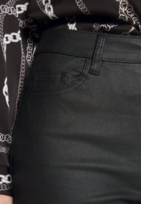 Czarne spodnie z ekoskóry o gładkiej teksturze, z zakrzywioną kieszenią i szlufkami, w połączeniu z bluzką z wzorzystego materiału.