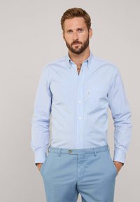 Camisa de botones a rayas azul y blanca con cuello puntiagudo y bolsillo en el pecho, combinada con pantalones azul claros, con una textura de tela suave.