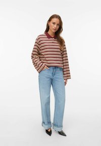 Polo de manga larga a rayas en burdeos y crema, combinado con jeans de pierna ancha azul claro y zapatos negros de punta afilada. Ajuste casual, look casual.