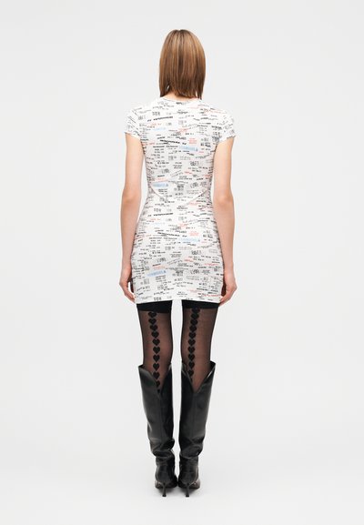 Balta mini suknelė su grafiniu spaudiniu, kuriame yra tekstas ir skaičiai. Derinama su juodomis permatomomis pėdkelnėmis ir juodais kelių aukščio batais.
