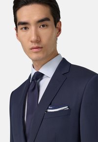 Jūrų mėtų švarkas su įpjovomis, derinamas su šviesiai mėlynu dryžuotu marškiniai ir tamsiai mėlyna kaklaraiščiu. Baltas kišeninis šalikas su mėlynomis juostelėmis švarko kišenėje.