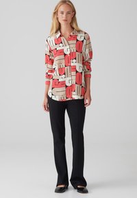 Langemouwshemel met een gedurfde grafische print in rood, beige en zwart. Gemaakt van een gladde stof, met een gekraagde halslijn en knoopsluiting.
