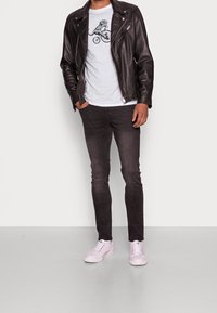 Černá kožená motorkářská bunda, šedé tričko s grafikou kola, tmavé džíny a růžové tenisky. Zobrazeno na neutrálním pozadí.