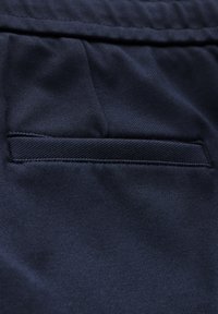 Tessuto blu navy con dettagli di tasche piatte e bordi di cucitura in contrasto. Texture liscia con una leggera lucentezza.