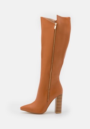 Botte haute en cuir marron clair avec talon aigu, bout pointu et fermeture éclair latérale, dotée d'un talon bloc empilé et d'une finition lisse.