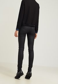 Černé skinny kalhoty z umělé kůže se hladkým povrchem a kontrastním šitím, spárované s černým svetrem a černými botami se cvočky.