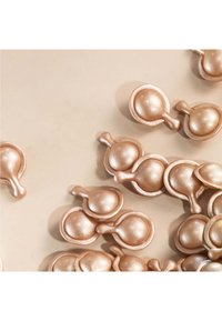 Capsule di crema color oro, dalla forma arrotondata e dotate di piccole maniglie, disposte su una superficie beige chiaro, che mostrano una texture liscia e lucida.