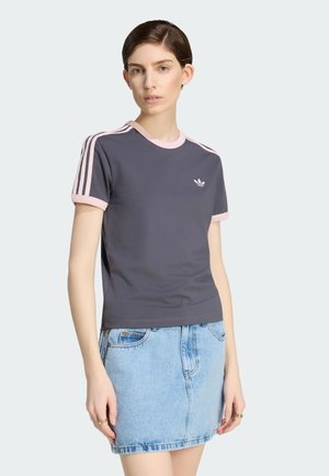 Vrouw draagt een donkergrijs Adidas T-shirt met roze bies en drie roze strepen op de mouwen, gecombineerd met een lichtblauwe denim rok.