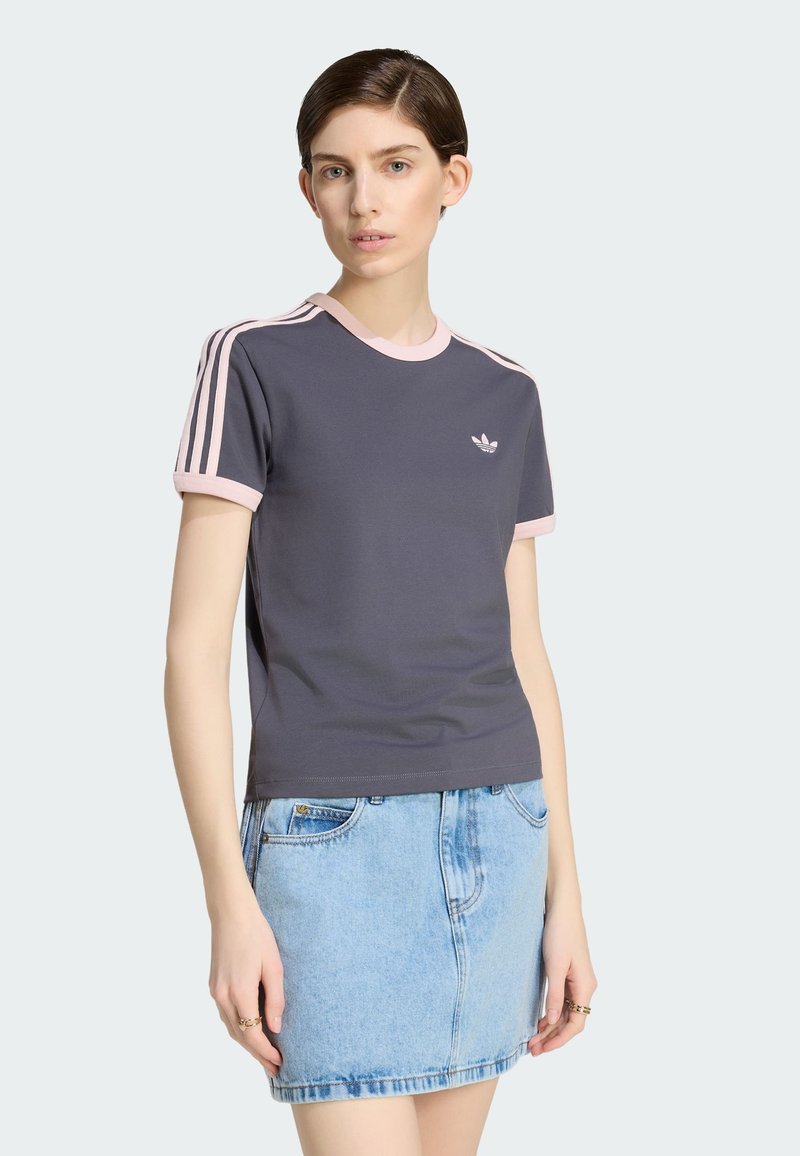 Kvinde iført en mørkegrå Adidas T-shirt med pink kant og tre pink striber på ærmerne, kombineret med en lyseblå denimskørt.