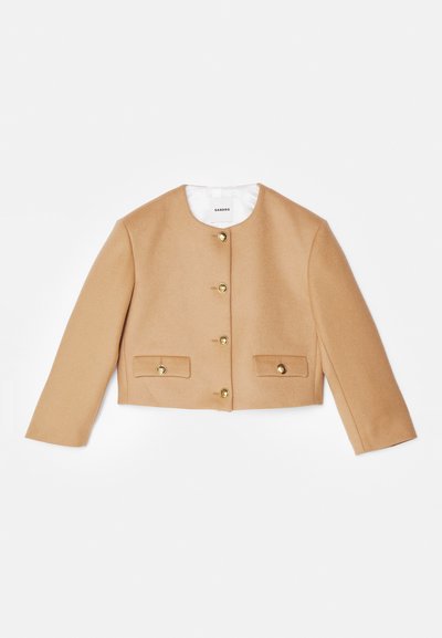 Veste beige raccourcie en laine avec un col rond, des boutons dorés et deux poches à l'avant. Dotée de manches longues et d'une texture lisse.