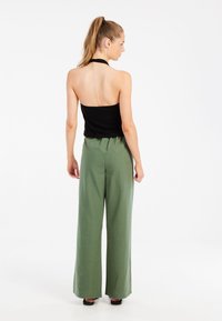 Top negro tipo halter y pantalones verdes de cintura alta y pierna ancha, con una textura suave y un ajuste relajado, vistos desde la espalda.