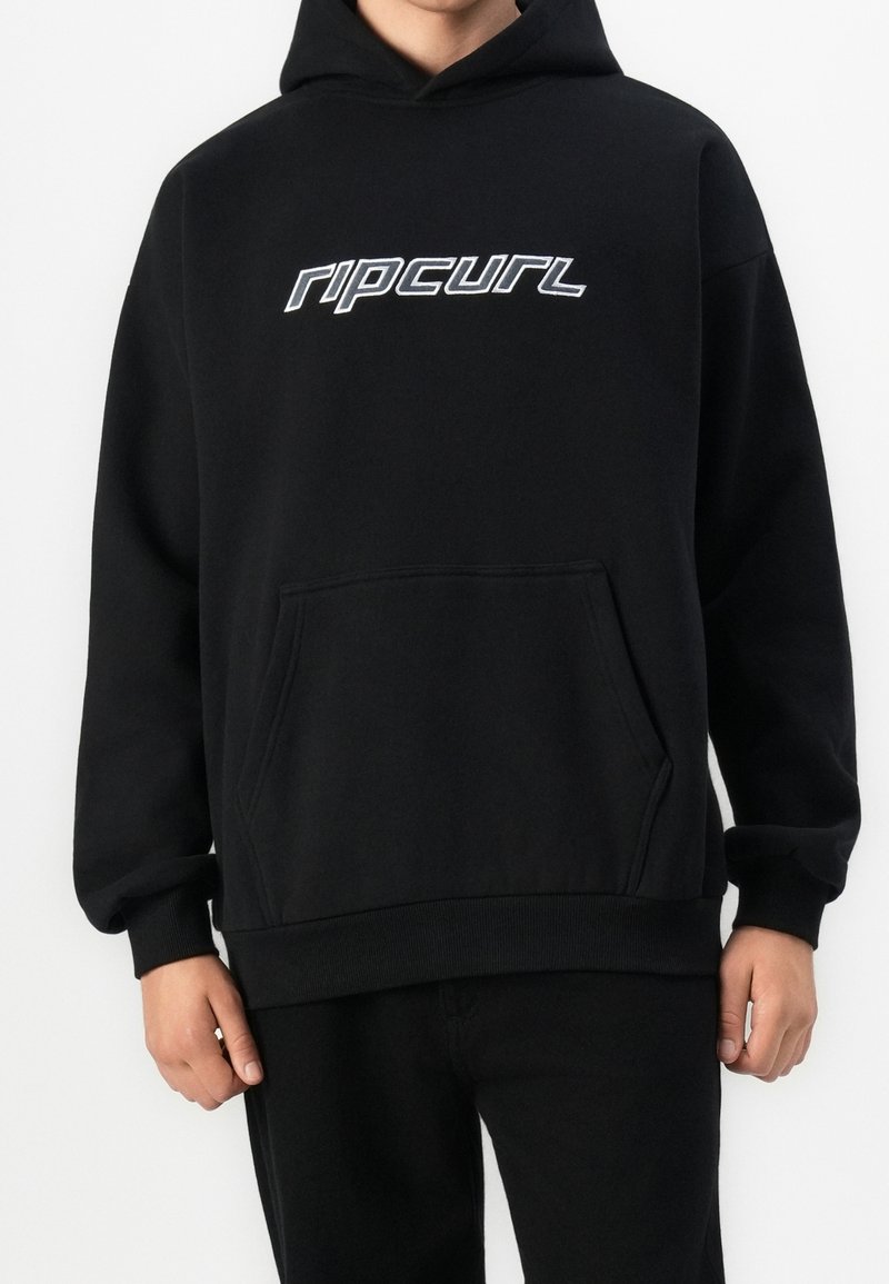 Personne portant un sweat à capuche noir avec une poche kangourou à l'avant et le logo "ripcurl" en texte blanc sur la poitrine.